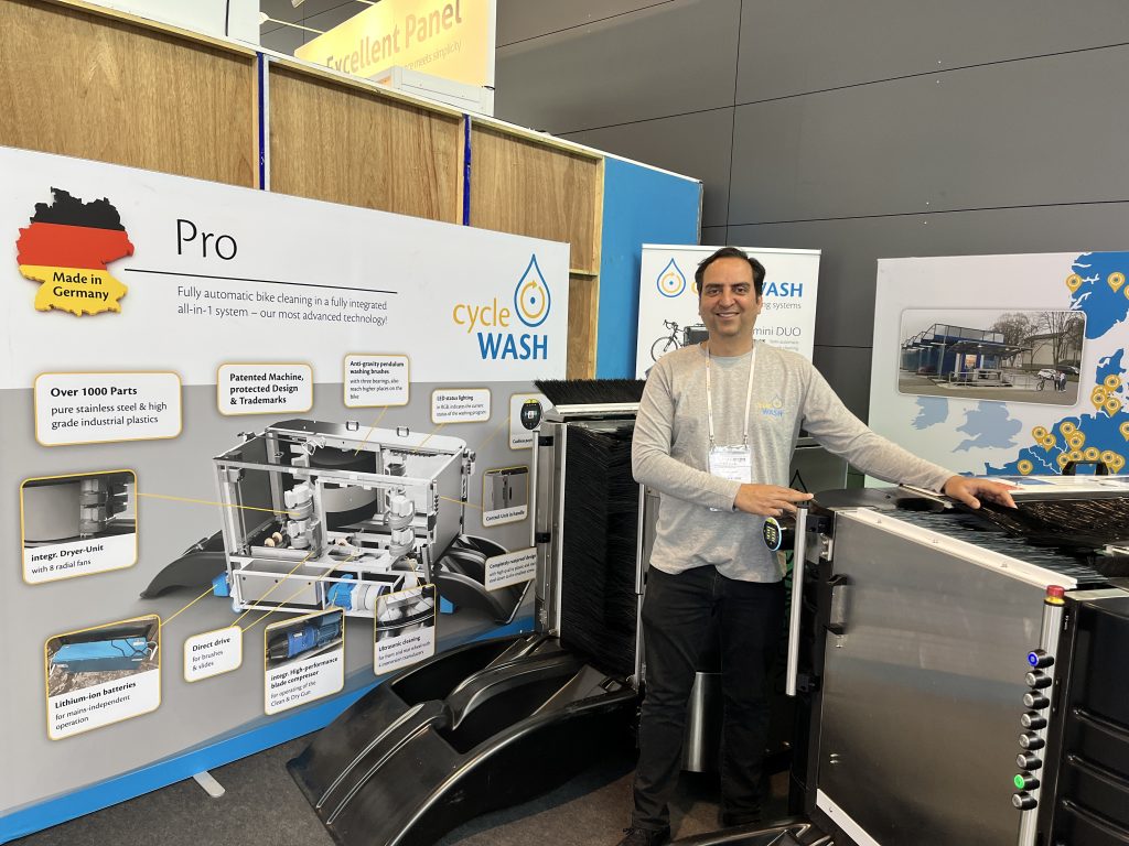 Sachin Kumar von cycleWASH steht neben einer Fahrradwaschanlage. Hinter ihm sind mehrere RollUps und Stellwände zu sehen.